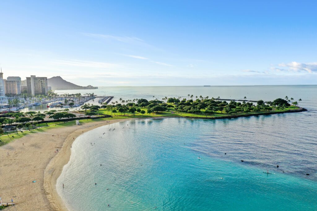Aerial shot of Honolulu with Diamond Head, marina, and sandy beach under a clear blue sky.