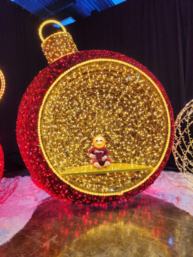 a baby sits inside a large decorative Christmas ornament